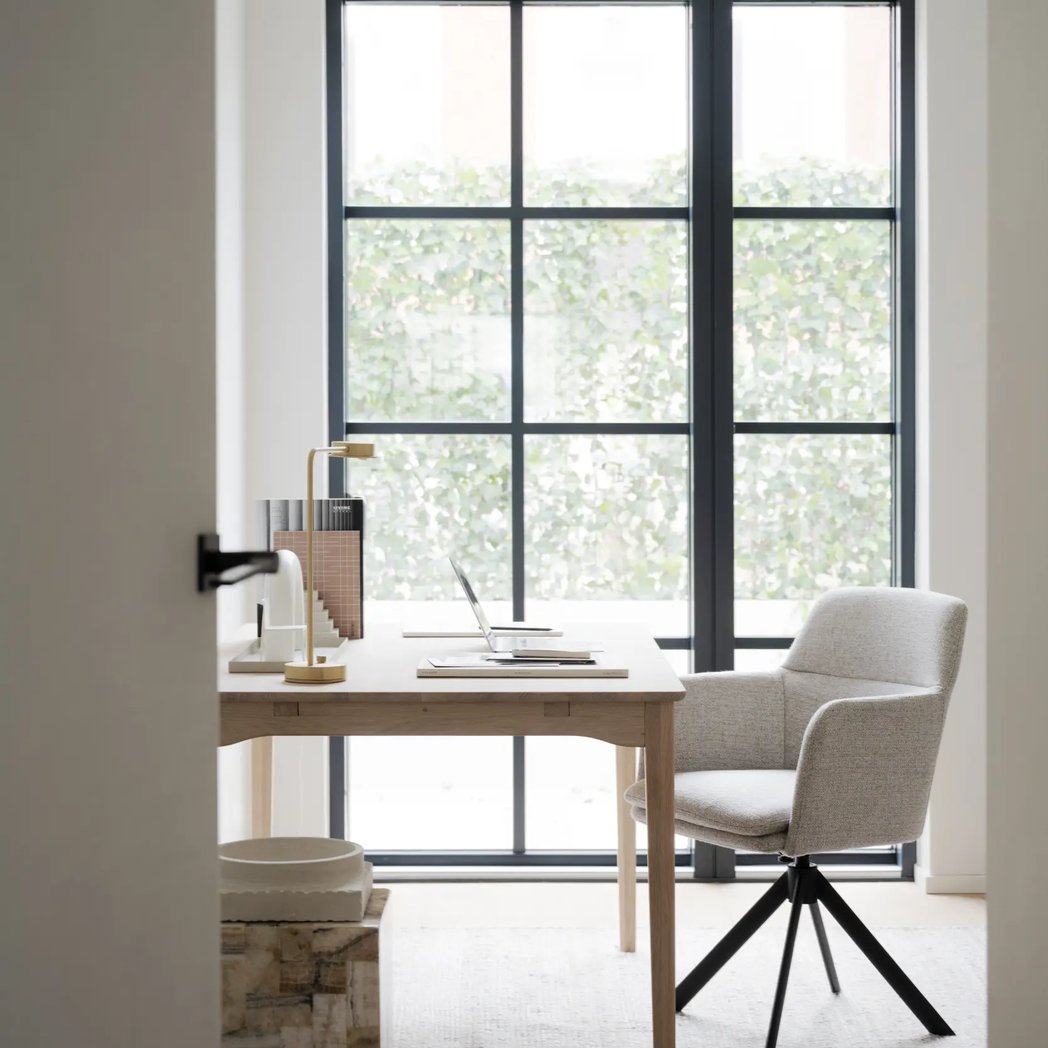 Rowico Gladstone spisebordsstol i lys beige stof ved et skrivebord i eg foran et stort sprossevindue