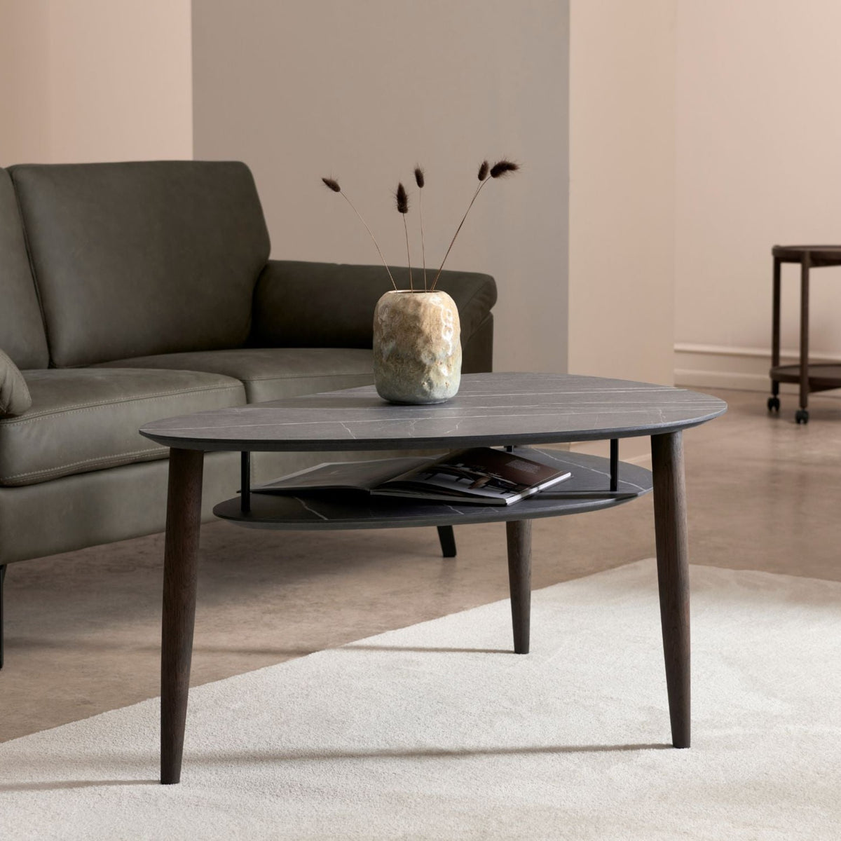 Thomsen Furniture Katrine sofabord med hylde i mørk stenlook laminat med røgfarvede egeben foran grøn sofa